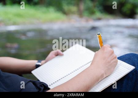 Cropped image of man writing in notebook ideas and enjoying nature in the park, while writing a book at campsite. Selective focus at object, back view Stock Photo