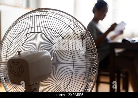 Sunny summer in front of the working fan, suffering from the summer heat. Unhappy Asian woman sitting in front of fan at work suffering from heat in m Stock Photo
