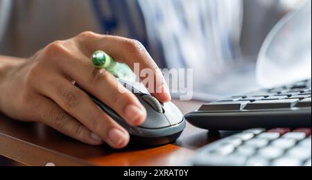 Woman using PC mouse while working on computer at table. Close up on hand of young woman sitting at wooden table in the office holding mouse of the la Stock Photo