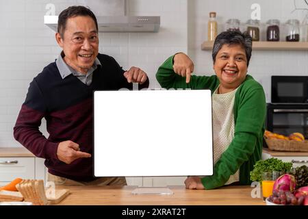 A retired couple shows off an empty laptop screen in the kitchen. Enjoy a relaxing retirement together. Free space for advertising communications. Stock Photo