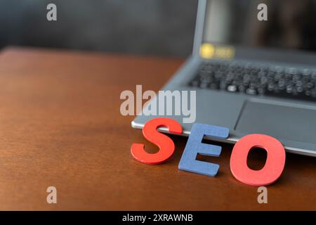 Wooden letter stands for SEO abbreviation lying on laptop at desk. Modern marketing buzzword SEO - Search engine optimisation. Top view on wooden tabl Stock Photo