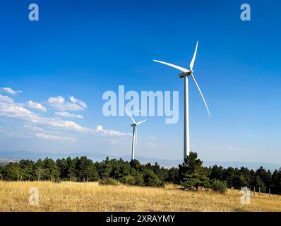 Modern windmills installed on hills in the countryside amidst vegetation. Stock Photo