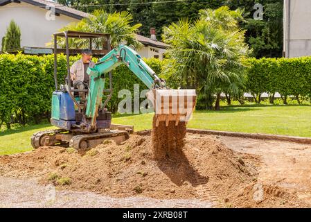 A worker on a mini excavator is digging the ground ahead of the house. Groundwork and exterior paving. Stock Photo