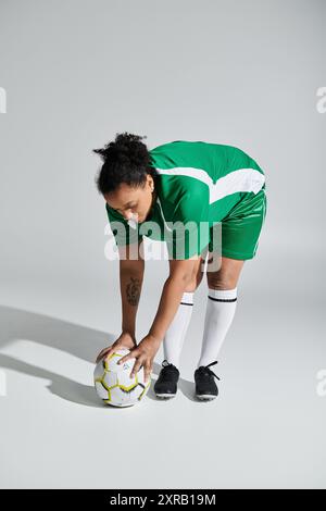 A woman in a green jersey bends down to the ground, preparing for a play during a football match. Stock Photo