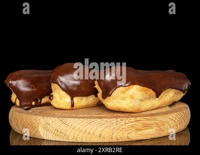 Three eclairs with cream on a wooden tray, macro, isolated on black background. Stock Photo