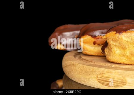 Three eclairs with cream on a wooden tray, macro, isolated on black background. Stock Photo