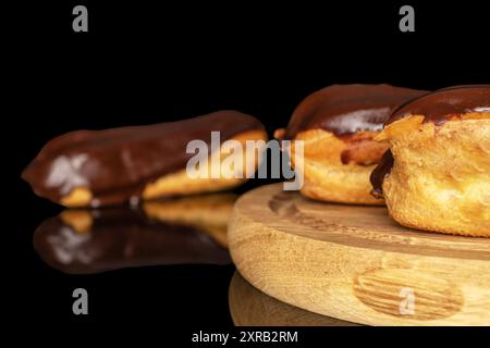 Three eclairs with cream on a wooden tray, macro, isolated on black background. Stock Photo