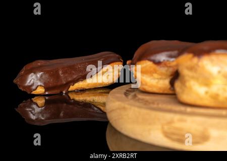 Three eclairs with cream on a wooden tray, macro, isolated on black background. Stock Photo