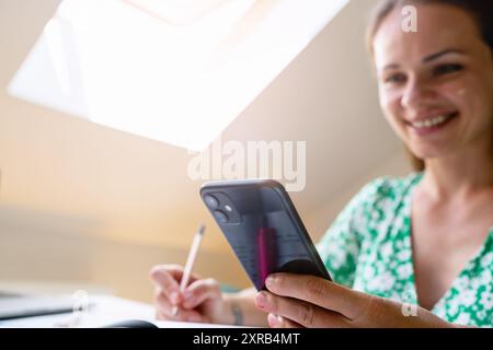 Woman sitting at a work desk, using a smartphone and smiling Stock Photo