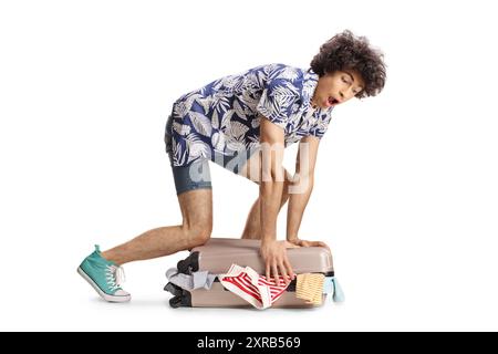 Funny young man with overpacked suitcase isolated on white background Stock Photo