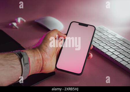 Hand holding smartphone with blank screen. Electronic devices on pink pastel background. Stock Photo