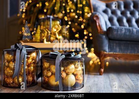 Luxurious interior of the room for Christmas and New Year. Living room in gray and gold tones with a sofa, many gifts, golden balls, ice lights, two C Stock Photo