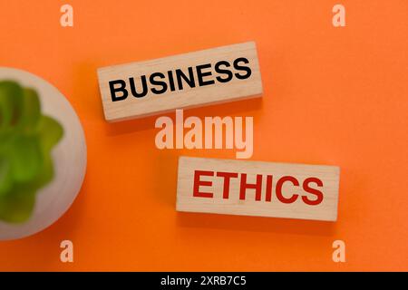 Wooden blocks spell out "business ethics" on a vibrant orange background. Stock Photo