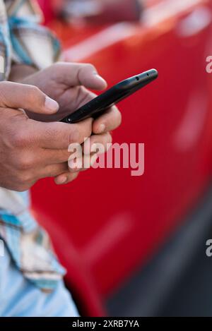 Close-up of man using phone outdoor - unrecognizable people with cellular smartphone chatting or texting with car in background - modern lifestyle with everywhere roaming connection Stock Photo
