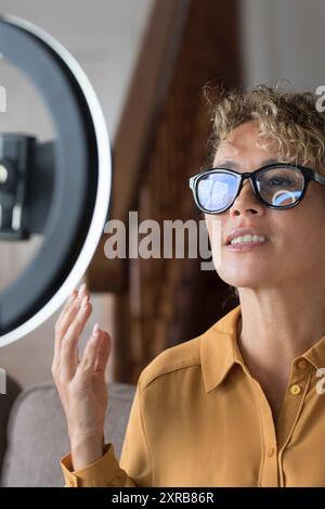 Young modern lady record live podcast with ring light and mobile phone to share on line on tutorial web page. Smart working freelance business caucasian woman in conference call Stock Photo
