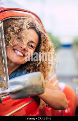 Portrait of cheerful happy adult pretty woman smile and enjoy driving car - caucasian female have fun outside the window of her vehicle - garden and road in background - people driving Stock Photo