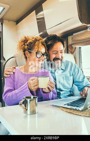Modern couple use together laptop inside camper van. Computer leisure people surfing the web. Traveler planning next destination smiling and enjoying freedom living off grid. Digital nomad concept Stock Photo