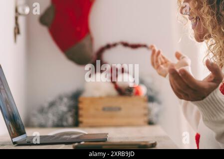 Happy woman using laptop at home to video call a friend during christmas holiday. Female people side portrait with santa claus hat and xmas decorations in background. People and modern technology Stock Photo