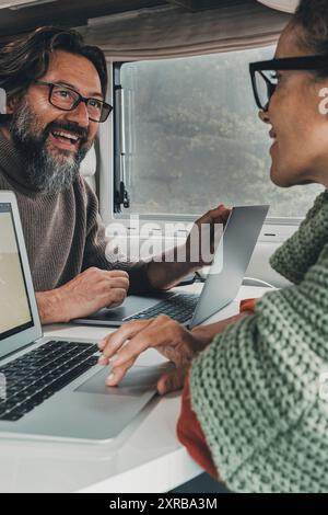 Digital nomad young couple working together inside a camper van using laptop computer. Happy free modern people man and woman in smart working travel activity. Online job and technology connection Stock Photo