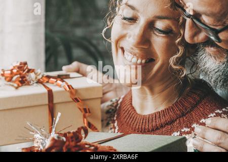 Love and christmas gifts concept leisure activity with young mature man and woman exchanging presents in winter holiday at home with smile and happiness. Couple in relationship hug and enjoy together Stock Photo