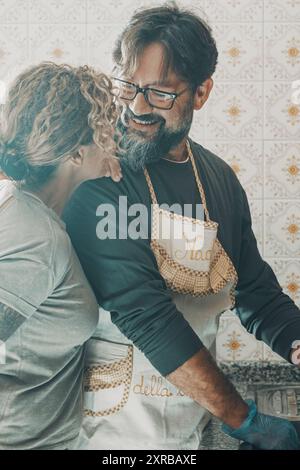 Happy couple adult people in love washing dishes together in the kitchen living at home sharing apartment. Married husband and wife doing housework with smile and happiness. Love lifestyle man woman Stock Photo