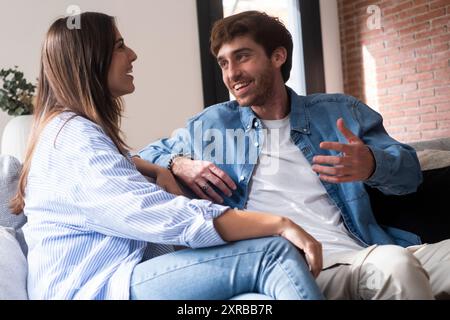 Cheerful millennial interracial lovers enjoying time together at home, happy arab man and indian woman sitting on couch in living room, embracing and having conversation. Love, family, relationship Stock Photo