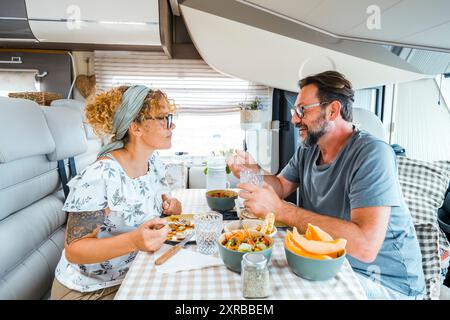 A happy couple spending time together having fun during vegetarian lunch inside a camper. People talking and sharing projects organizing the next destination. Stock Photo