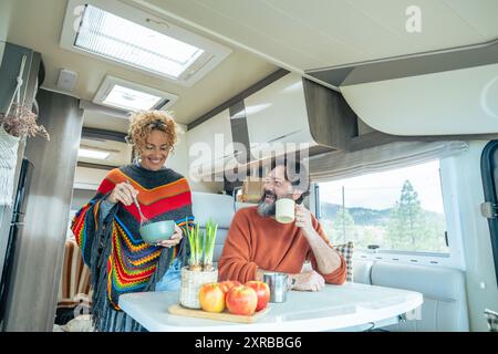 Youth mature couple enjoy life in a camper van motorhome together in indoor leisure activity. Nature view outside the window. Happy traveler people man and woman inside a van for vacation holiday Stock Photo