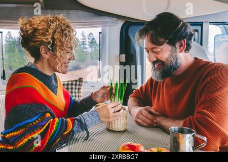 Youth mature couple enjoy life in a camper van motorhome together in indoor leisure activity. Nature view outside the window. Happy traveler people man and woman inside a van for vacation holiday Stock Photo