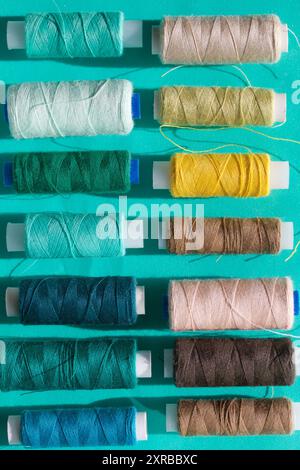Spools of different colors are arranged in a row on a turquoise background. In the style of flat lay. Stock Photo