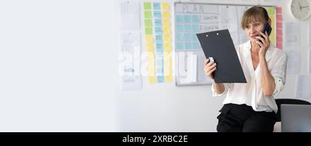 Senior businesswoman discussing documents over phone in office Stock Photo