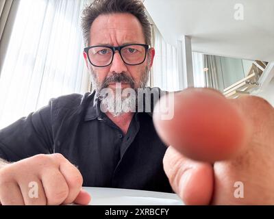 Laptop camera view of adult man ready to click the screen with doubts expression. Online scam and fraud websites. Security password choice. Hacked computer pov. Mature using laptop worried no skills Stock Photo