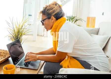 Couple lifestyle at home using laptop modern new business concept. One woman using computer sitting on sofa and man in the background at the table. Apartment indoor leisure. Hotel room travel people Stock Photo