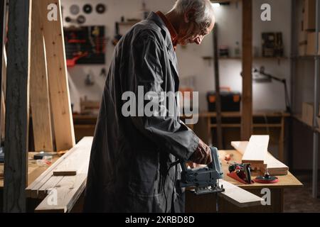 Elderly Carpenter Cutting Wooden Board with Jigsaw Stock Photo