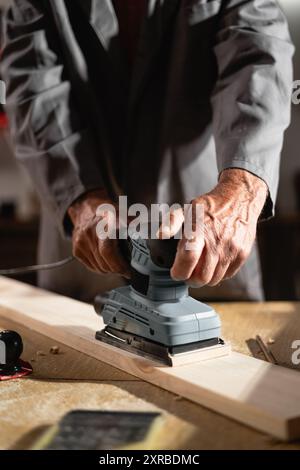 Close-up of Carpenter Using Belt Sander to Sand Wooden Board in Woodworking Workshop Stock Photo