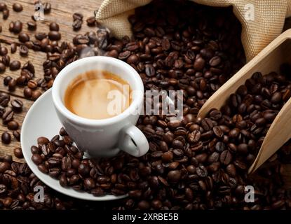 Coffee cup with burlap sack of roasted beans on rustic table Stock Photo