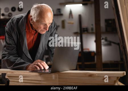 Elderly Man Using Laptop in His Small Business Workshop Stock Photo