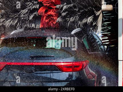 Black car in automatic car wash rotating red and black brush. Washing vehicle. Stock Photo