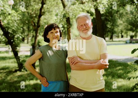 Portrait of smiling senior couple standing in green park and posing for photo Stock Photo