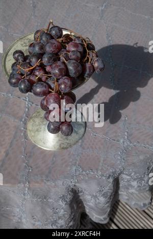 Still life with dark red grapes on a blue-grey transparent delicate lace blanket in the sunlight Stock Photo