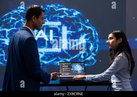 IT staff members solving tasks on laptop device, running artificial intelligence programming scripts. Indian workers using notebook to write lines of code for AI applications development Stock Photo