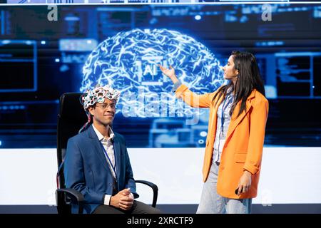 Professionals speaking at tech conference, explaining impact of neural implants and AI tech. Neuroscience researchers present risks and threats associated with EEG headsets usage Stock Photo