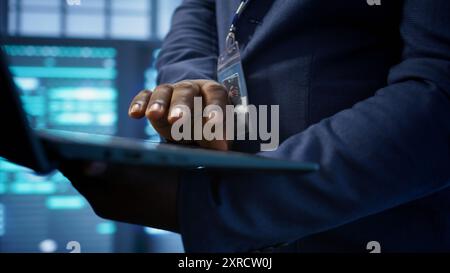 IT technician working on notebook in data center, overseeing server operations. Extreme close up shot of man ensuring optimal performance and data integrity in server hub, camera B Stock Photo