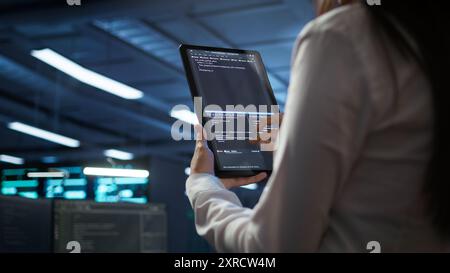 Data center software developer responsible for installation of networking equipment solving tasks on device. Close up of woman doing maintenance on server room infrastructure using tablet, camera B Stock Photo