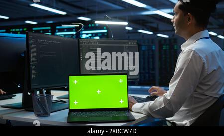 Admin in data center using isolated screen laptop to design, implement and manage gear, ensuring optimal performance and reliability. Expert in server room coding on chroma key notebook, camera B Stock Photo