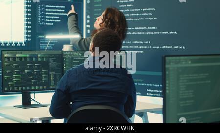 Governmental hackers analyzing data for cyber threat detection, looking at a big screen in high tech office. Highlight cyber intelligence, online security and prevention of digital threats. Camera A. Stock Photo
