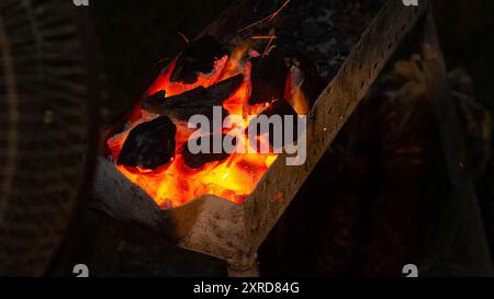 Burning ember charcoal in a fireplace for grill meat and fanned with an electric fan. wood charcoal for grilled sate. Stock Photo