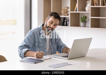Positive Hispanic entrepreneur man using laptop for working in office Stock Photo