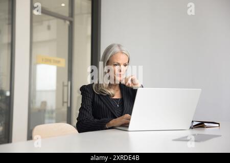 Focused elder company executive woman in suit working at laptop Stock Photo