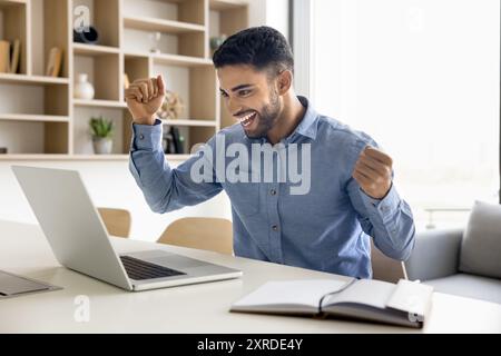 Cheerful young Arab manager man celebrating win at laptop Stock Photo